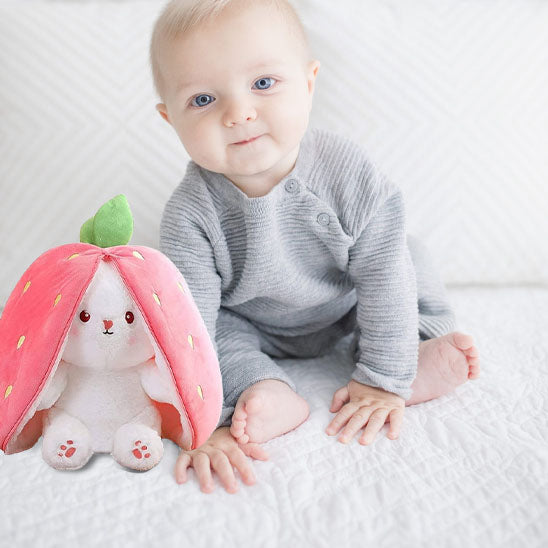 bébé assis et la peluche lapin fraise à côté de lui