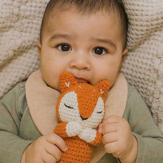 bébé allongé au lit  tient doudou renard marron 