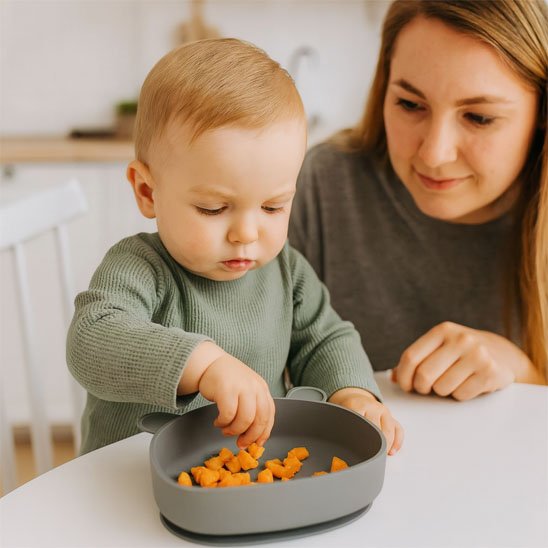 Assiette bébé ventouse maman regarde le bébé qui mange dans son assiette avec les mains